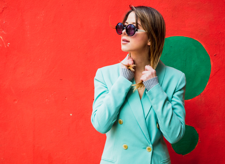 Young woman in Blazer of 90s style and sunglasses in red background.の写真素材