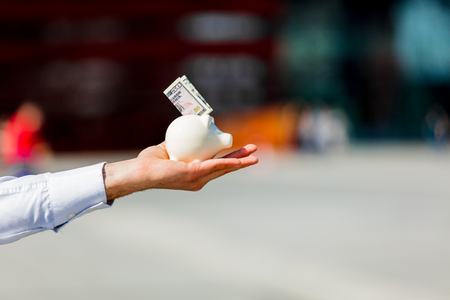 Male's hand holding piggy bank with cash dollars at outdoor in spring timeの写真素材