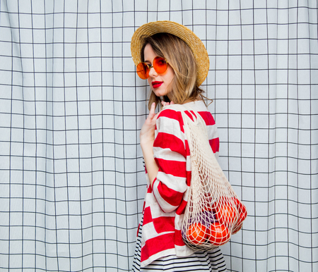 Portrait of a young smiling woman in hat and striped jacket with net bag on checkered background