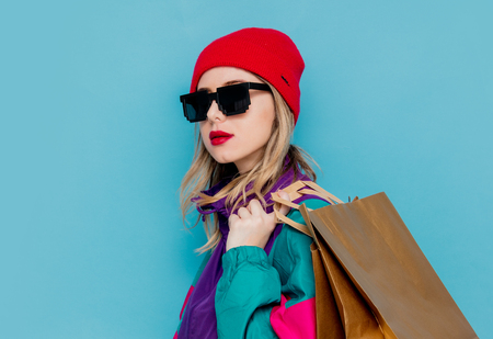 Portrait of a woman in red hat, sunglasses and suit of 90s with shopping bags on blue and pink background.の写真素材