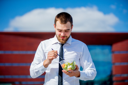 Young businessman in shirt and tie with salad lunch box on outdoor in sunny day.の写真素材