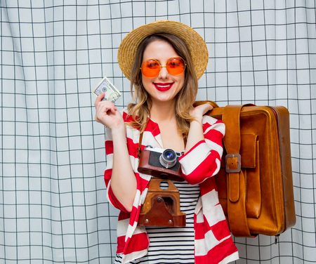 Portrait of a young smiling woman in hat and striped jacket with vintage camera, suitcase and...