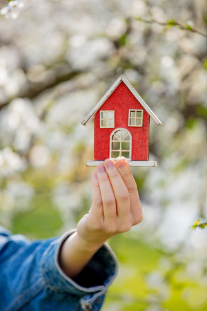 Female hand holding red little house near flowering tree. Spring seasonの写真素材