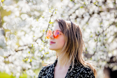 Young girl in a sunglasses stay near a flowering tree in the park. Spring seasonの写真素材