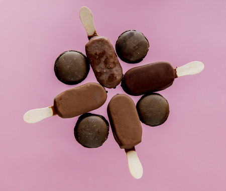 Chocolate ice lollys and french macrons on pink background. Objects without of a shadows