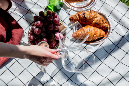Female holding a wine glasses for a date on checked cloth with grape and croissants. Side viewの写真素材