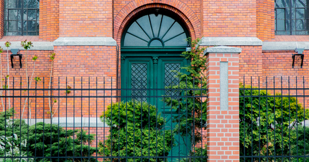 Door with arch in old brick building of Victorian era with fence and bush.