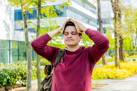 Young upset student with book on head stay near modern building of University. Spring time seasonの写真素材