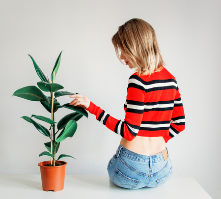 young woman in sptriped sweater and jeans sitting on a table near ficusの写真素材