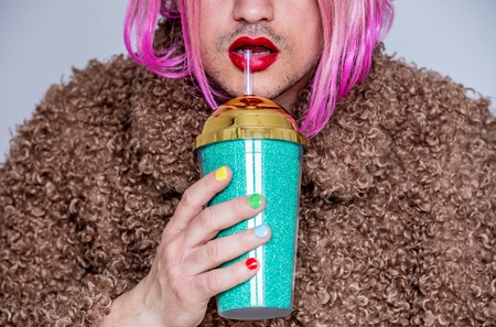 transvestite man with lipstick and polish nail holding cocktailの写真素材