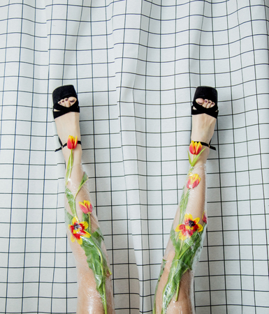 woman holds her legs up wrapped with cellophane and tulips flowers.