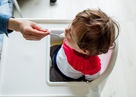 Mother feeds a little toddler boy with a spoon during lunch in the room.の写真素材