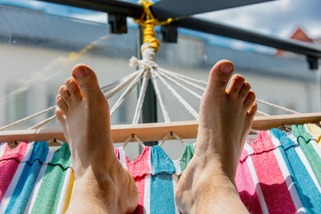 Legs of a man lying on a hammock on a balcony in the cityの写真素材