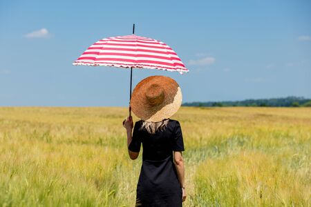 Female in black dress and hat with red umbrella stay in wheat fieldの写真素材