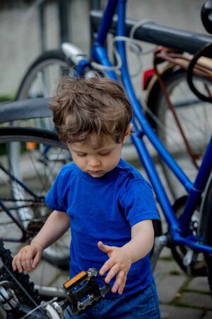 little toddler boy plays enthusiastically with big bikes on a city bike parkingの写真素材