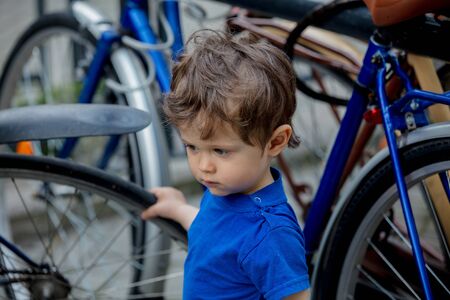 little toddler boy plays enthusiastically with big bikes on a city bike parkingの写真素材