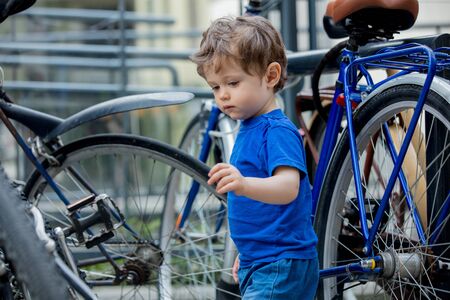 little toddler boy plays enthusiastically with big bikes on a city bike parkingの写真素材