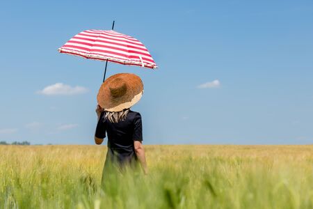 Female in black dress and hat with red umbrella stay in wheat fieldの写真素材