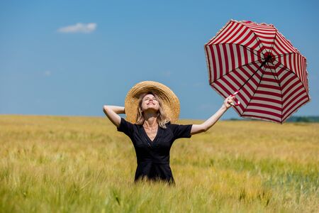 Female in black dress and hat with red umbrella stay in wheat fieldの写真素材