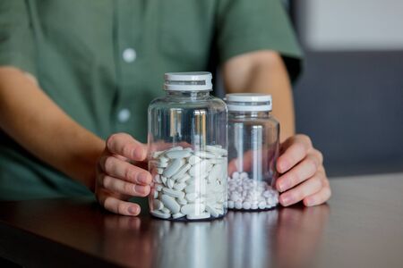 Woman's hand holding two jars of white pills on a table at homeの写真素材
