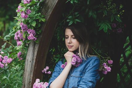 Young woman near bush of purple flowers in a garden. Side view