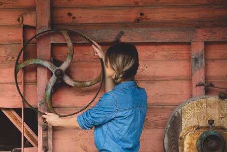 Young woman near wheel of an old wooden combine harvester of XIX century. Side viewの写真素材