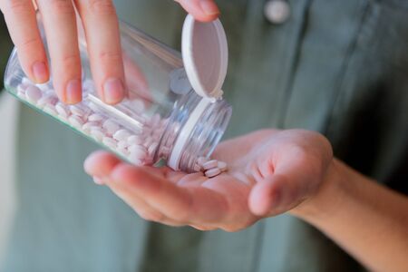 Woman pours white pills from a transparent jar into her hand.の写真素材