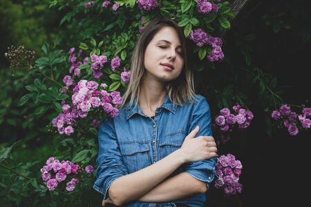Young woman near bush of purple flowers in a garden. Side viewの写真素材