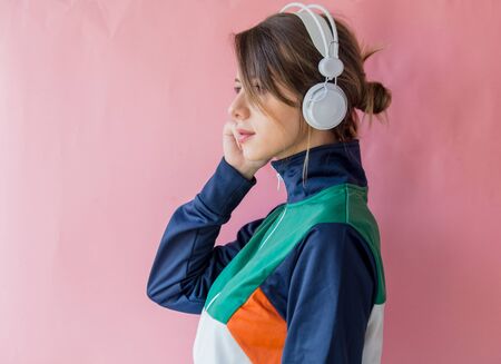 Young woman in 90s style clothes with headphones on pink backgroundの写真素材