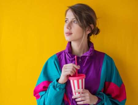 Young woman in 90s style clothes with cup on yellow backgroundの写真素材