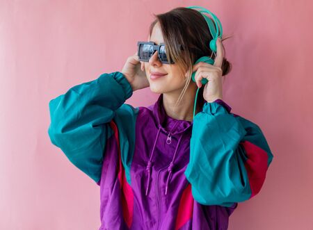 Young woman in 90s style clothes with headphones on pink background