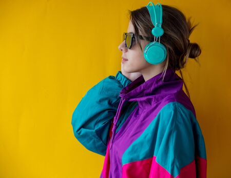 Young woman in 90s style clothes with headphones on yellow backgroundの写真素材