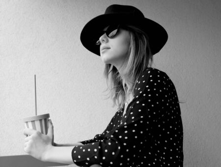 Young woman in hat and sunglasses with a drink.
