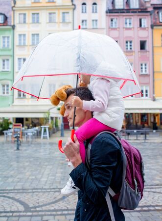 Little girl with umbrella sits on her fathers shouldersの写真素材