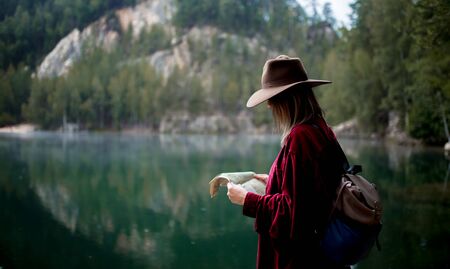 Young woman in hat and red shirt with map near lake