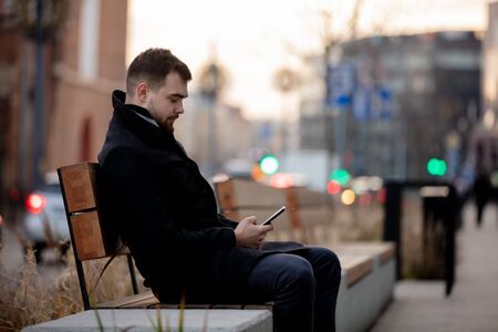 young man with a mobile phone is sitting on a benchの写真素材