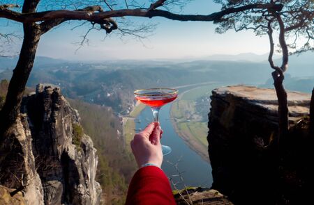 woman's hand holds a glass of champagne against the background of the Elbe river in Saxon...