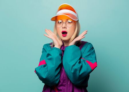 Style blonde woman in 80s glasses and hat on blue background