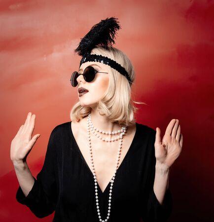 Beautiful blonde woman in twenties years clothes and sunglasses on red background
