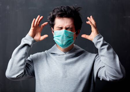 young white man in protective mask with headache on dark background
