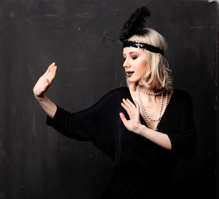 Beautiful blonde woman in twenties years clothes dancing on dark background
