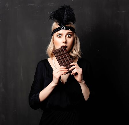 Beautiful blonde woman in twenties years clothes with chocolate slice on dark background