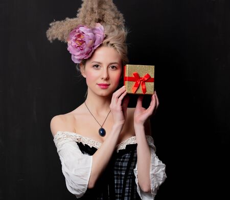 Beautiful blonde countess with a gift box on dark background