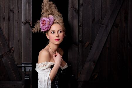 Beautiful blonde countess with vintage hairstyle and corset on dark background