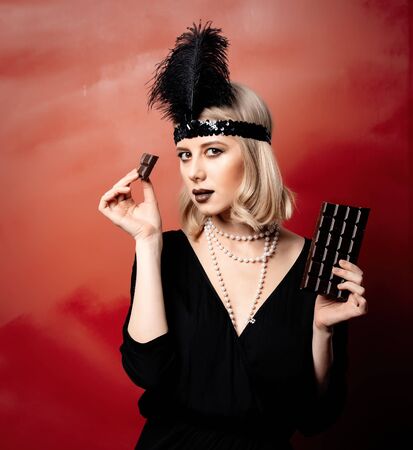 Beautiful blonde woman in twenties years clothes with chocolate slice on red background