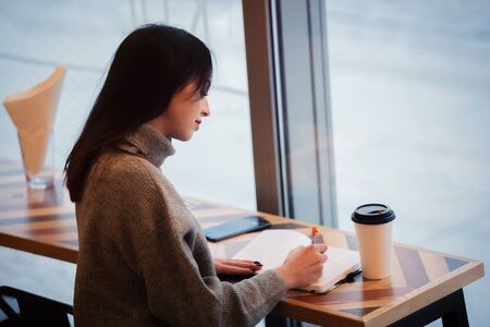 Brunette woman with notebook is working in a cafe
