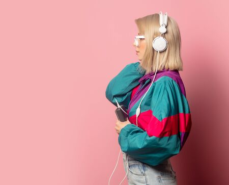Beautiful blonde woman in 90s clothes with headphones on pink background