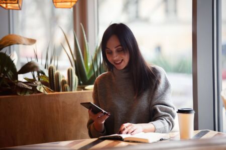 Brunette woman with notebook and mobile phone is working in a cafe
