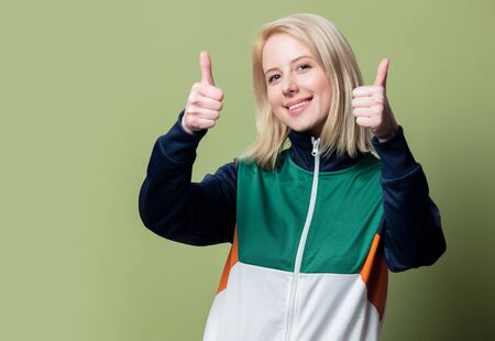 Beautiful blonde woman in 90s sport suit show OK gesture on green background