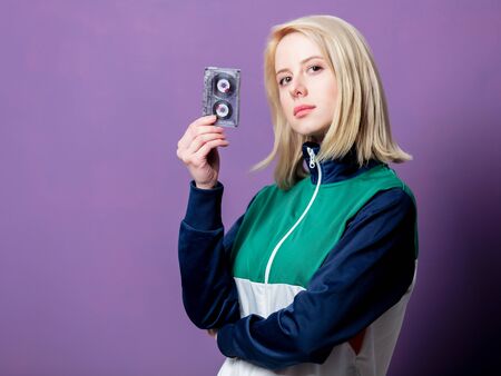 Style blonde woman in 80s clothes with tape cassette on purple background